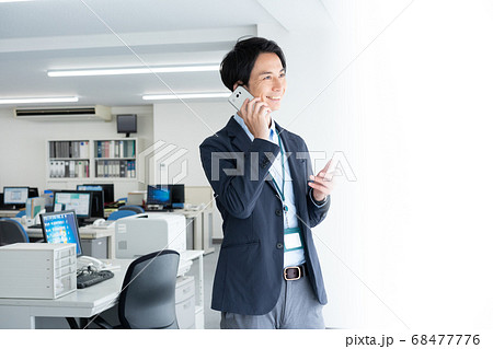 早朝1人でオフィスに出社してスマホで話をする若いビジネスマン 早朝1人でオフィスに出社してスマホで話をする若いビジネスマン 68477776