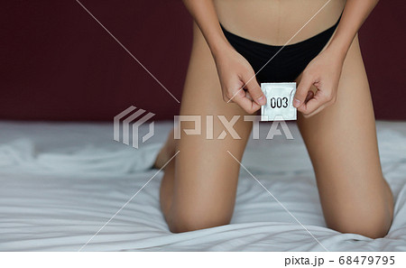 Young sexy woman hands in black underwear holding condom number 003 on bed in hotel bedroom Young sexy woman hands in black underwear holding condom number 003 on bed in hotel bedroom 68479795