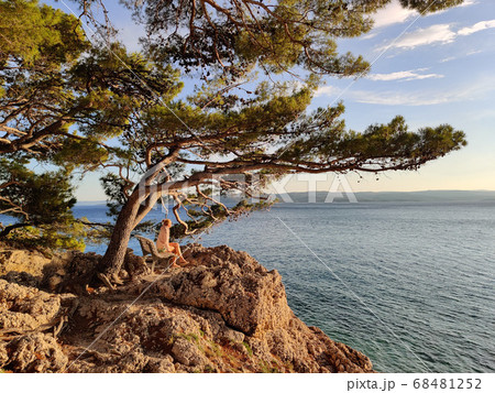 Pensive woman on vacations, sitting and relaxing under large pine tree on bench by dip blue sea enjoying beautiful sunset light in Brela, Makarska region, Dalmatia, Croatia Pensive woman on vacations, sitting and relaxing under large pine tree on bench by dip blue sea enjoying beautiful sunset light in Brela, Makarska region, Dalmatia, Croatia 68481252