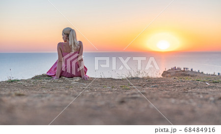 A joyful adult girl with a Caucasian appearance looks at the sunset with her back in the summer in the evening A joyful adult girl with a Caucasian appearance looks at the sunset with her back in the summer in the evening 68484916