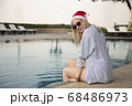 Girl in a red Christmas hat next to the swimming pool with blue water. Holiday concept. 68486973