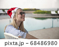 Girl in a red Christmas hat next to the swimming pool with blue water. Holiday concept. 68486980