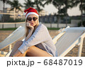 Girl in a red Christmas hat on the beach next to the sea. Holiday concept. 68487019