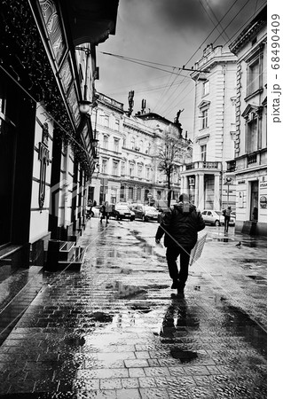 After rain. Lviv/Ukraine - January 30, 2020: A delivery man carries an empty box along the Les Kurbas Street. 68490409