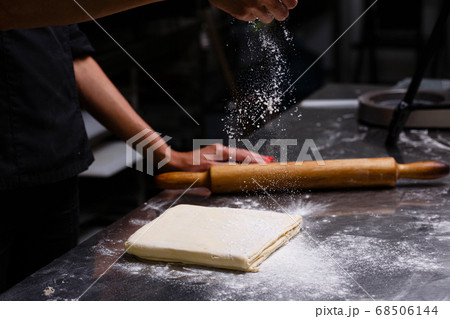 The chef prepares pastries in a professional kitchen. Dark background. 68506144