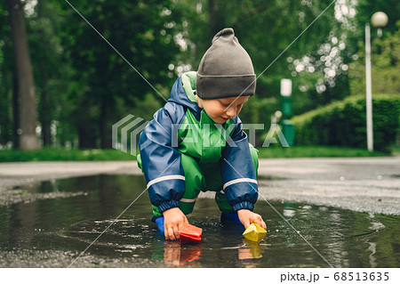 Funny kid in rain boots playing in a rain park 68513635