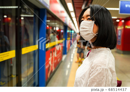 young adult Asian woman wearing a face mask on subway playform waiting for train 68514437