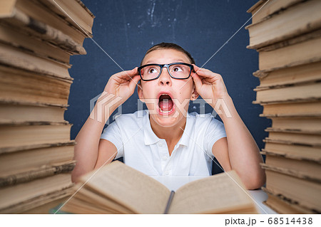 Smart boy in glasses getting crazy of reading book while sitting between two piles of books Smart boy in glasses getting crazy of reading book while sitting between two piles of books 68514438