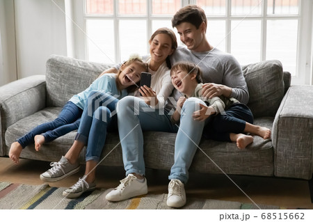 Smiling young couple showing funny video on phone to kids. Smiling young couple showing funny video on phone to kids. 68515662