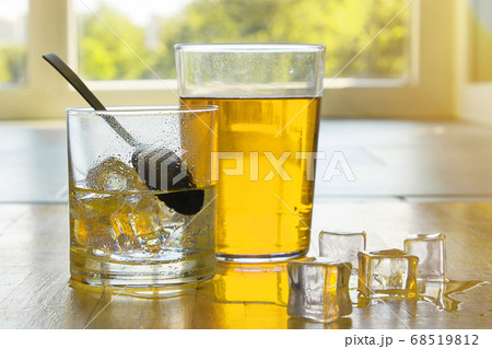 Red and black tea and lemonade in a transparent glass with ice on a background of a sunny window. 68519812