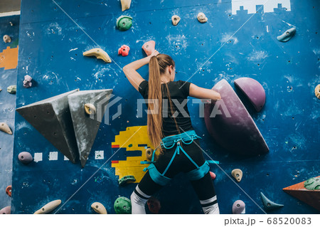 Young woman climbing a tall, indoor, man-made rock climbing wall 68520083