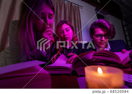 Two women and a guy are reading a mysterious books, close view 68520084