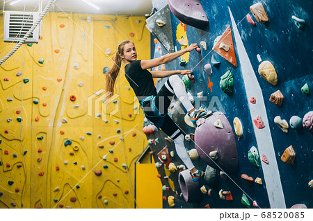 Young woman climbing a tall, indoor, man-made rock climbing wall 68520085