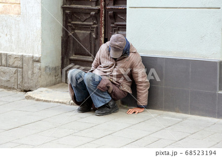 poor homeless man sitting near the wall of thewall of the building. poor homeless man sitting near the wall of thewall of the building. 68523194