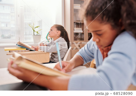 Pensive schoolgirl with open book thinking of answer to question on blackboard Pensive schoolgirl with open book thinking of answer to question on blackboard 68528090