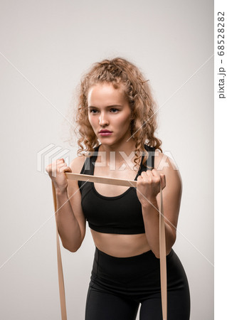 Young sportswoman with blond curly hair exercising with elastic band in gym 68528282