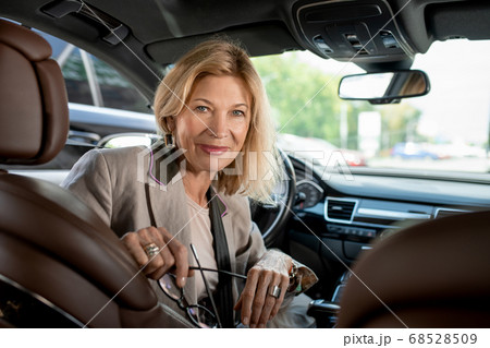 Happy mature female sitting by steer in car and looking at someone on backseat Happy mature female sitting by steer in car and looking at someone on backseat 68528509