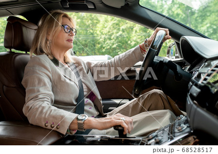 Businesswoman sitting by open window in car and driving to office for meeting Businesswoman sitting by open window in car and driving to office for meeting 68528517