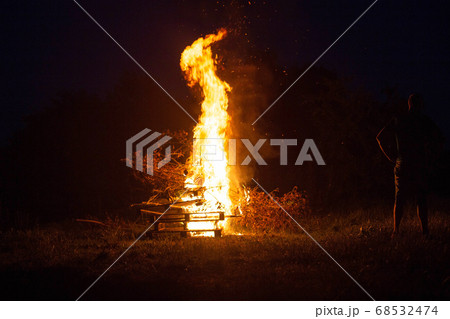 Beautiful big bonfire in the forest at night. A man looks at a bonfire, outdoor recreation, background, tourist 68532474