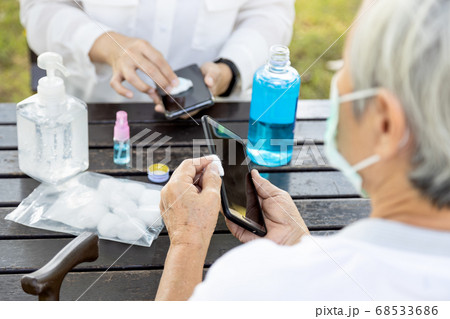 Cleaning mobile phone to eliminate germs,Covid-19,asian women cleaning the phone by hand sanitizer gel,elderly people using alcohol to wipe to avoid contamination,disinfection,outbreak of Coronavirus 68533686