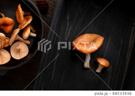 Raw fresh mushroomon on cast-iron pan left, and two mushrooms on right, on wood background. Top view, space for text 68533936