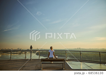 Blonde woman in headphones sitting on bench under blue sky Blonde woman in headphones sitting on bench under blue sky 68536130