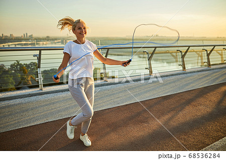 Cheerful woman jumping over skipping rope outdoors Cheerful woman jumping over skipping rope outdoors 68536284