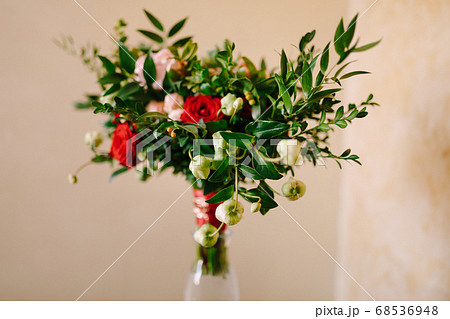 bridal bouquet of red and pink roses, boxwood branches, not blooming buds of white flowers and red ribbons with brooch in the glass vase bridal bouquet of red and pink roses, boxwood branches, not blooming buds of white flowers and red ribbons with brooch in the glass vase 68536948