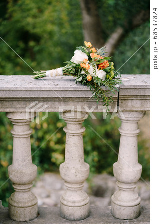 bridal bouquet of white and orange roses, eringyum, ammi, boxwood branches, alstroemeria with white ribbons on the railing of an ancient staircase 68537824