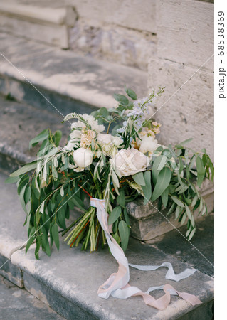 bridal bouquet of white and cream peonies, roses, veronica, branches of eucalyptus tree with white ribbon on the ancient staircase 68538369