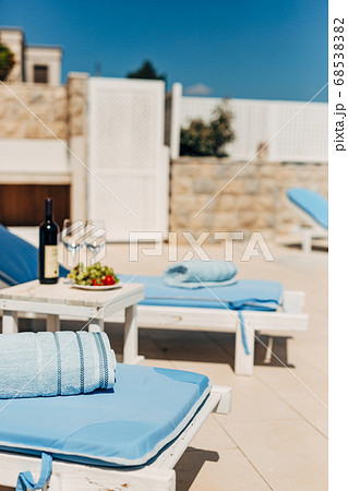 Blue towels on sun loungers on the beach. Table with wine, glasses and grapes. Blue towels on sun loungers on the beach. Table with wine, glasses and grapes. 68538382