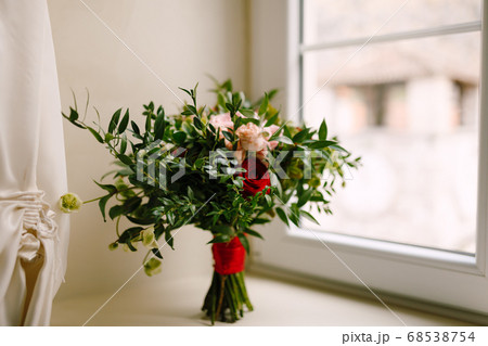 bridal bouquet of red and pink roses, boxwood branches, not blooming buds of white flowers and red ribbons on the window 68538754