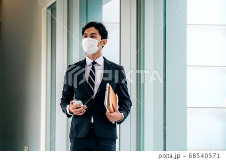 オフィスの廊下でスマホを操作するマスクをしたスーツ姿のビジネスマン 68540571