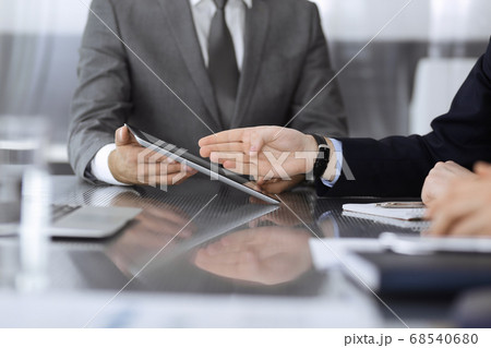 Unknown businessman using tablet computer and working together with his colleague while sits at the glass desk in modern office. Teamwork and partnership concept Unknown businessman using tablet computer and working together with his colleague while sits at the glass desk in modern office. Teamwork and partnership concept 68540680