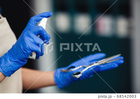 Master in medical gloves spraying disinfectant on scissors, close up 68542003