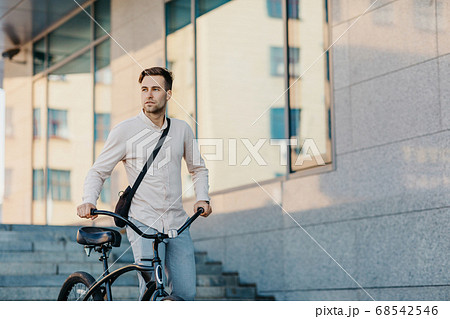 Fast eco city transport. Serious young guy in business clothes, walks with bike at city 68542546