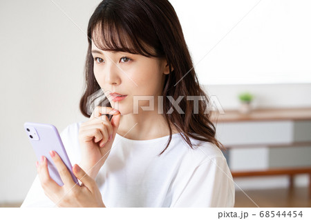 リビングでスマホを操作する不安顔の若い女性 リビングでスマホを操作する不安顔の若い女性 68544454