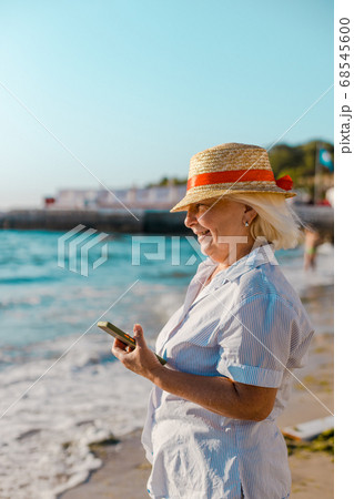 Summer holiday background. Caucasian blond woman in straw hat and striped shirt makes photo by smartphone of the sea on a sunny day. Summer holiday background. Caucasian blond woman in straw hat and striped shirt makes photo by smartphone of the sea on a sunny day. 68545600