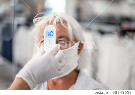 Hand holding infrared thermometer to measuring temperature on blurred woman with face mask on background. Corona virus, Covid-19, quarantine or virus outbreak concept Hand holding infrared thermometer to measuring temperature on blurred woman with face mask on background. Corona virus, Covid-19, quarantine or virus outbreak concept 68545655