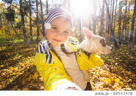 Little girl taking selfie with her dog at autumn park. Child posing with jack russell terrier for a picture on the mobile phone outdoors. Pet and children concept. 68547476
