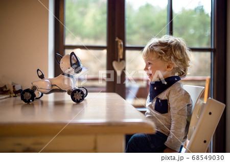 A cute toddler boy sitting indoors at home, playing with robotic dog. 68549030