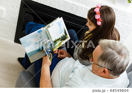 Granddaughter and grandfather watching photos together in a photo album at home 68549604