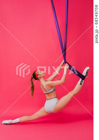 Full length body size view portrait sexy attractive strong sporty young womant gymnast in retro swimsuit hangs on air silk stretch out in split looking up isolated over pink red background Full length body size view portrait sexy attractive strong sporty young womant gymnast in retro swimsuit hangs on air silk stretch out in split looking up isolated over pink red background 68549708