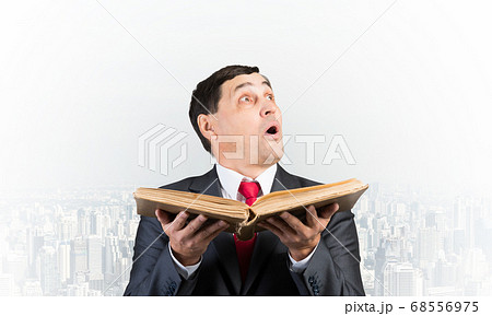 Surprised businessman holding open old book Surprised businessman holding open old book 68556975