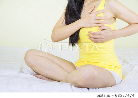 Woman hand checking lumps on her breast for signs of breast cancer sitting on bed in bedroom, healthy lifestyle female,healthy girl medical awareness cancer prevention concept 68557474