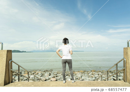 Young fitness healthy woman stand and rest listening to music on headphones after before running or jogging in the beach in sunshine on beautiful summer day. Sport fitness training outdoor concept. Young fitness healthy woman stand and rest listening to music on headphones after before running or jogging in the beach in sunshine on beautiful summer day. Sport fitness training outdoor concept. 68557477