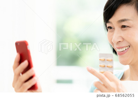 スマホとクスリを見るミドル女性 68562055