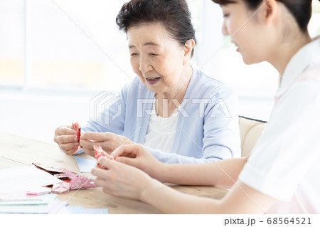 介護イメージ　折り紙を折るシニア女性と介護士 68564521