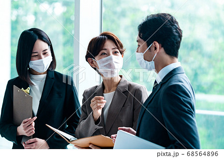オフィスでミーティングするマスクをしたスーツ姿の男女ビジネスマン 68564896