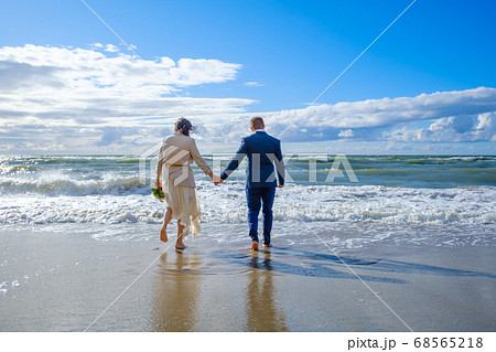 Unrecognizable bride and groom walking towards sea Unrecognizable bride and groom walking towards sea 68565218